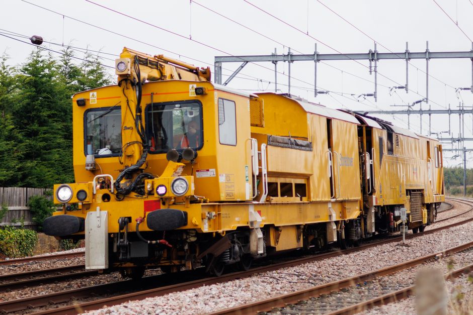 Imagem de um trem de manutenção ferroviária amarelado em uma linha de trem, representando infraestrutura e transporte ferroviário.