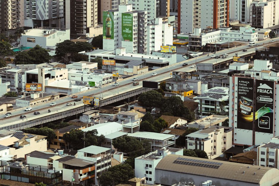 Imagem de uma vista urbana com prédios residenciais e comerciais, evidenciando a movimentação do transporte na cidade.