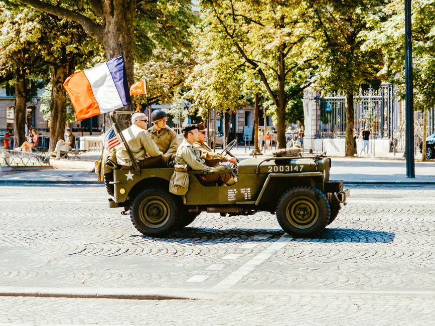 Soldados históricos em viagem de recreio em uma praça arborizada, remetendo à memória militar e ao patriotismo.
