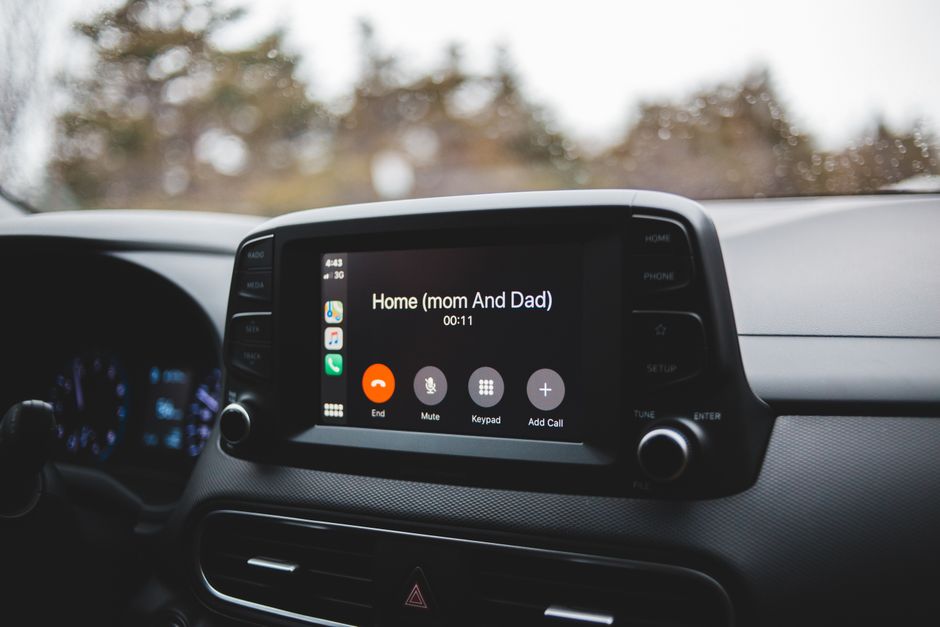 Tela de sistema de som de carro exibindo uma chamada em andamento, com o ambiente externo visível através do para-brisa.