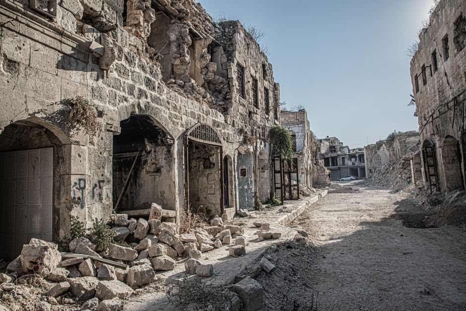 Imagem de uma rua abandonada e destruída, com construções em ruínas e sinal de deterioração urbana.