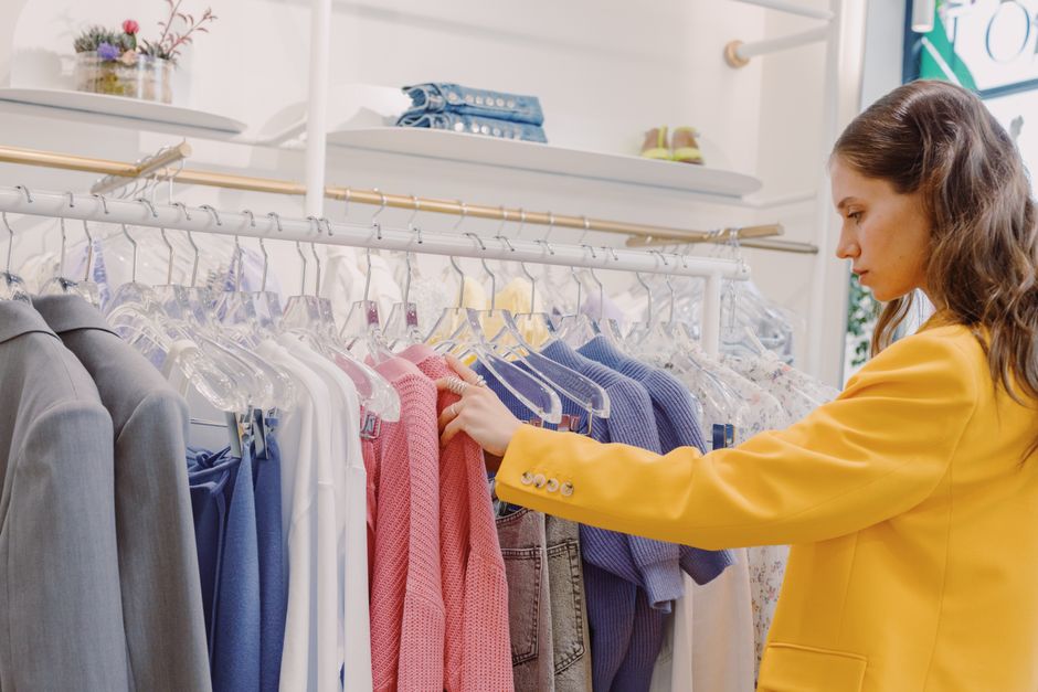 Mulher analisando roupas em uma loja de moda feminina, focada na seleção de peças e estilo.
