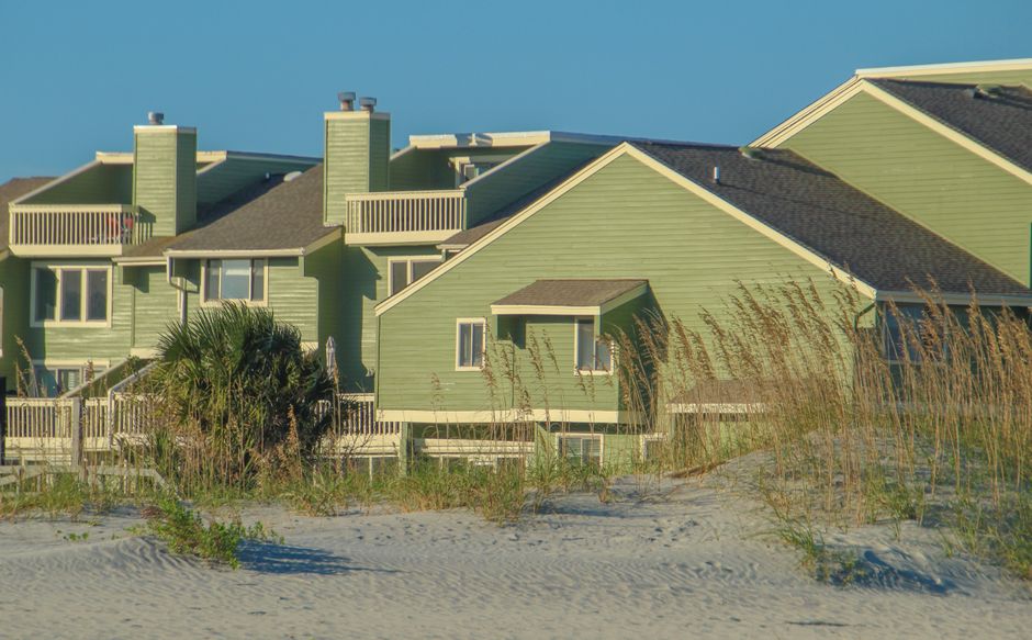 Conjunto de casas coloridas na área costeira, com vegetação de praia ao redor.