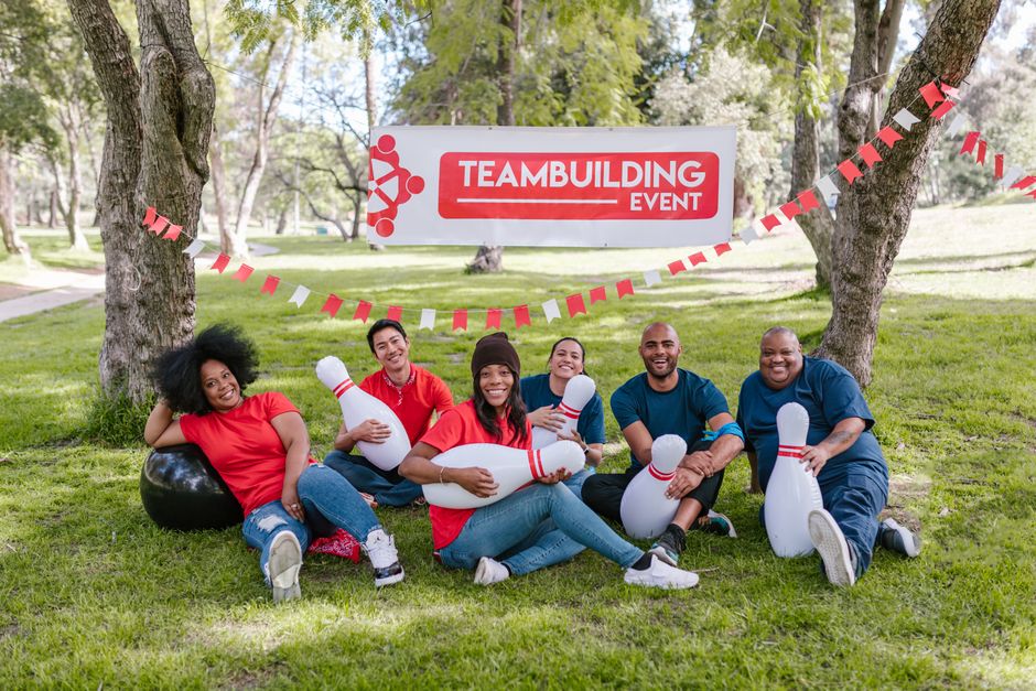 Grupo de pessoas participando de um evento de trabalho em equipe ao ar livre, com decoração temática relacionada ao tema de teambuilding.