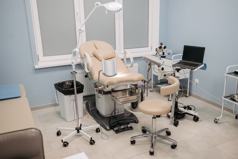 Sala de exame ginecológico equipada com cadeira, instrumentos médicos e computador, ideal para um blog de saúde feminina.