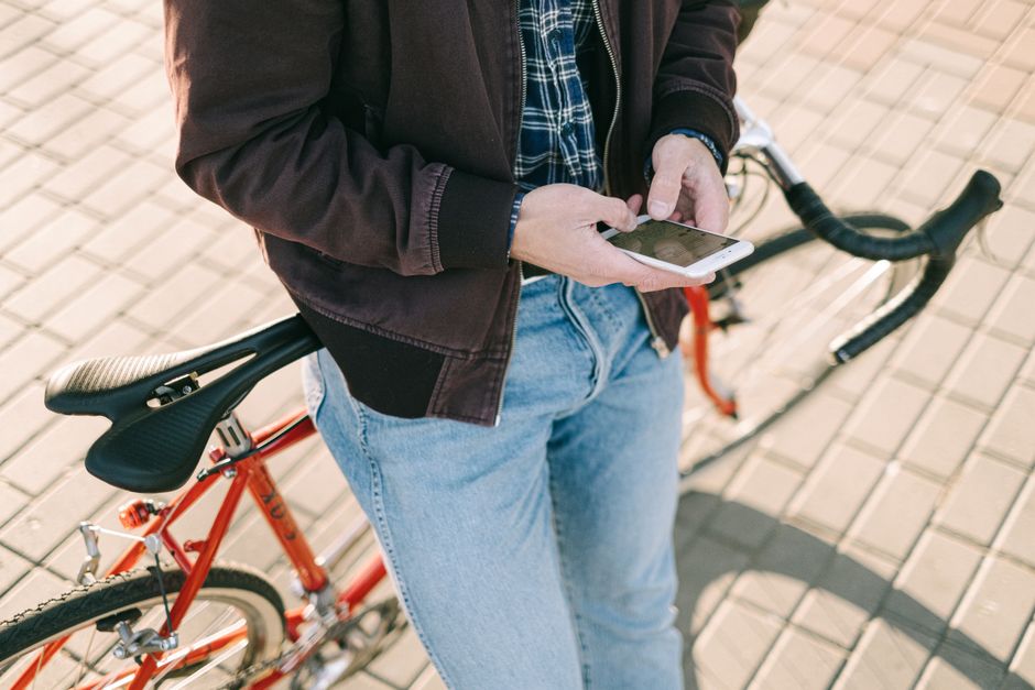 Pessoa usando smartphone ao lado de uma bicicleta em um ambiente externo, ilustrando mobilidade e uso de tecnologia.