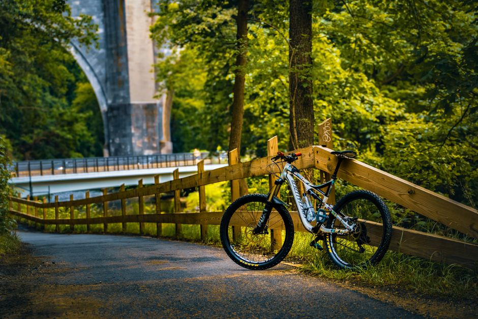 Ciclista descansando ao lado de uma bicicleta em trilha em meio à natureza, sob iluminação natural durante o dia.