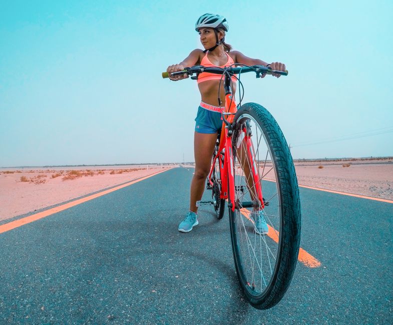 Mulher de bicicleta em uma estrada deserta sob céu claro, simbolizando liberdade e aventura ao ar livre.