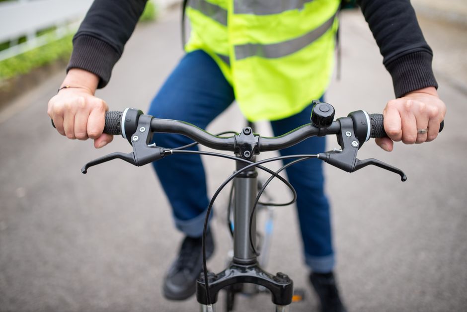 Pessoa vestida com colete de segurança pedalando uma bicicleta em ambiente urbano, destacando a mobilidade sustentável.