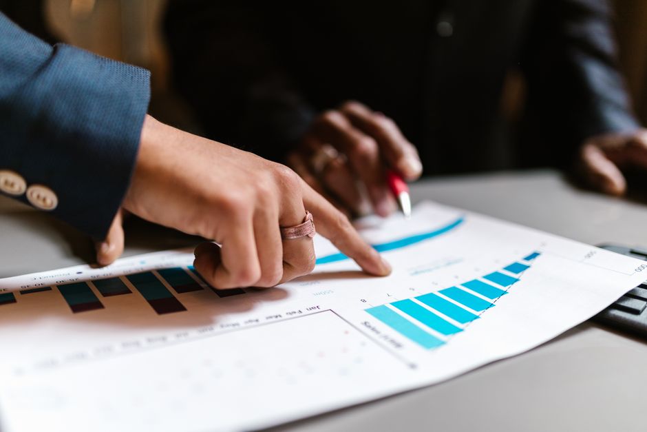 Pessoas analisando gráficos e dados financeiros em uma reunião de negócios, destacando a estratégia e tomada de decisões corporativas.