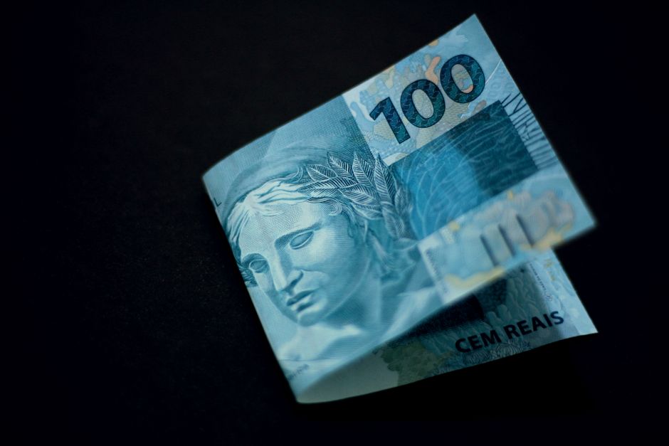 Nota de cem reais dobrada sobre fundo preto, simbolizando questões de dinheiro e economia.