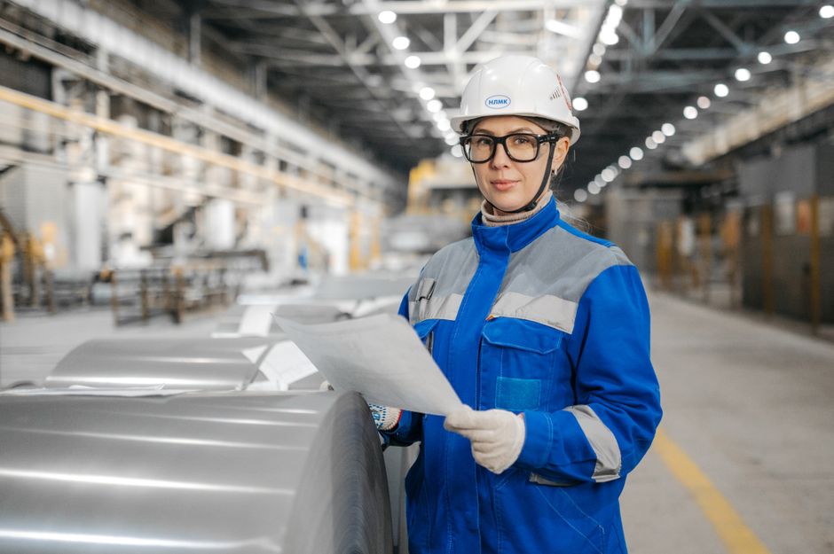 Profissional de engenharia ou supervisora avaliando documentos em um ambiente industrial ou de produção.