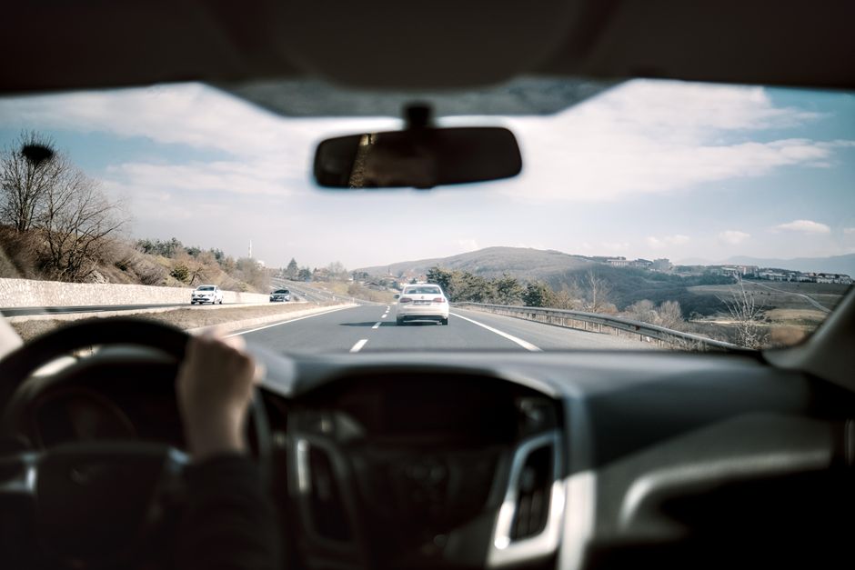 Imagem de uma viagem de carro por uma estrada em um cenário rural, com paisagens de morros e céu parcialmente nublado, destacando o tema de deslocamento e aventura.