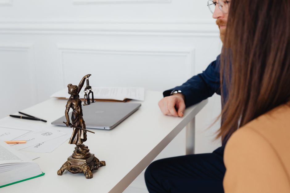 Imagem que representa uma conversa ou reunião relacionada à área jurídica ou financeira, com uma estátua da Justiça em destaque na mesa.