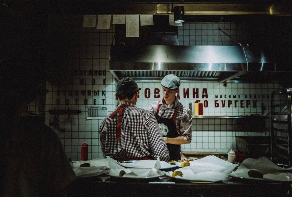 Dois funcionários de restaurante conversando na cozinha, com iluminação suave e ambiente de trabalho organizado.