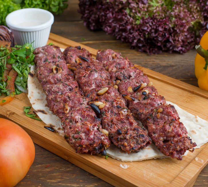 Prato de kibe tradicional servido em uma tábua de madeira, acompanhado de molho branco e hortaliças, ideal para um artigo sobre culinária árabe ou receitas típicas.