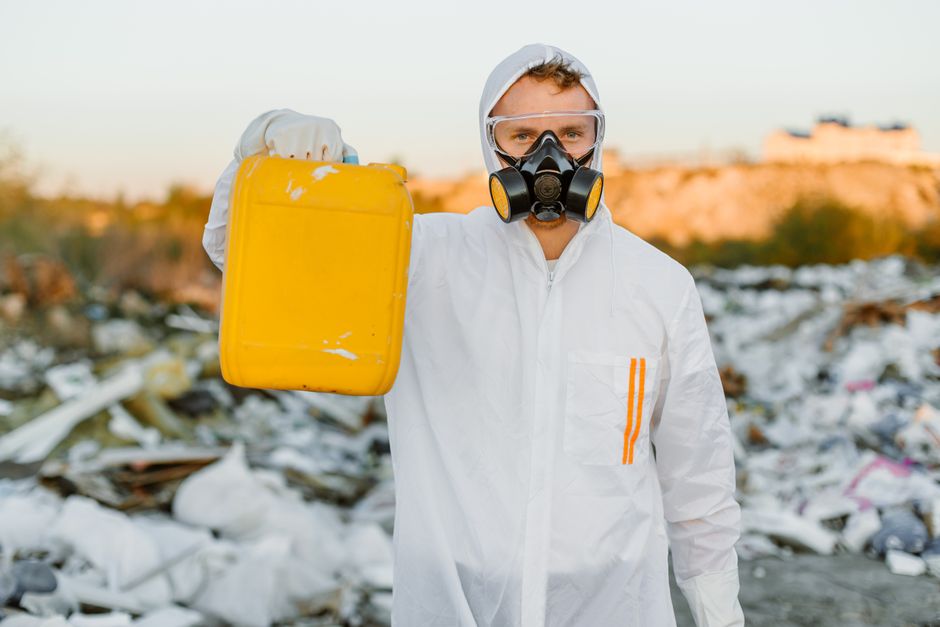 Pessoa com equipamento de proteção pessoal em ambiente de descarte de resíduos, destacando a importância da gestão ambiental e do descarte correto de lixo.