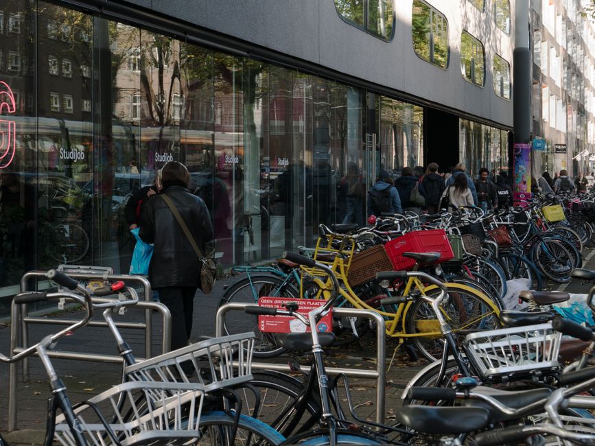 Imagem de pessoas esperando em frente a uma loja com várias bicicletas estacionadas na rua, no contexto de mobilidade urbana e transporte alternativo.