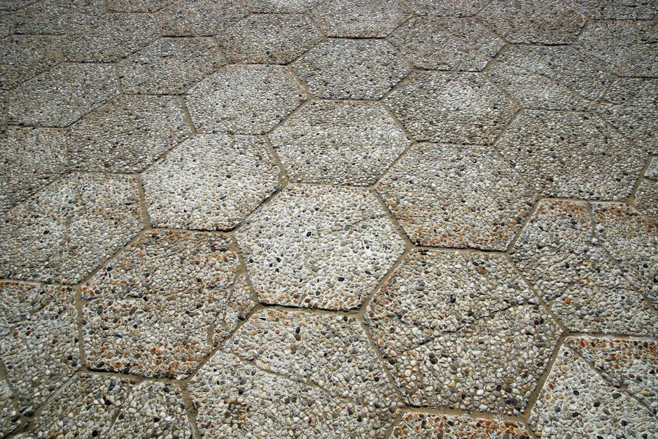Imagem de piso de paralelepípedos de pedra, com superfície texturizada e detalhes de calcário e cascalho, ideal para ilustrar temas de urbanização ou conservação de espaços públicos.