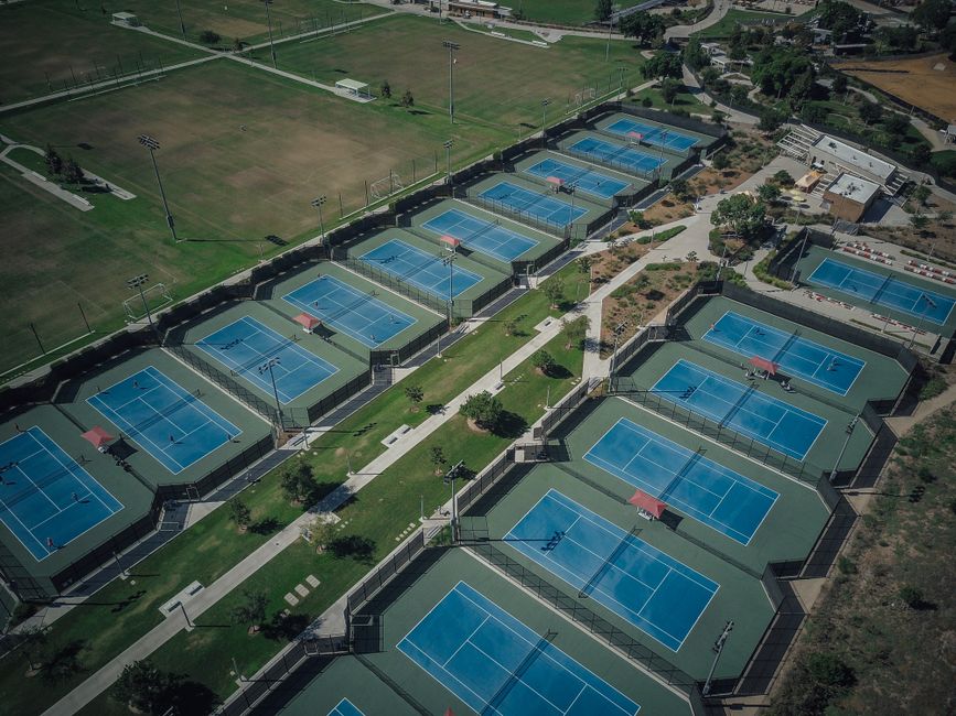 Imagem aérea de várias quadras de tênis em um complexo ao ar livre, com destaque para as áreas de jogo e iluminação.
