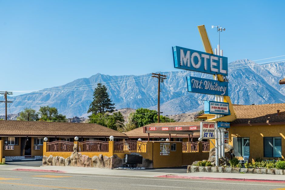 Imagem de um motel em uma cidade com montanhas ao fundo, destacando a sinalização do estabelecimento e o ambiente externo.