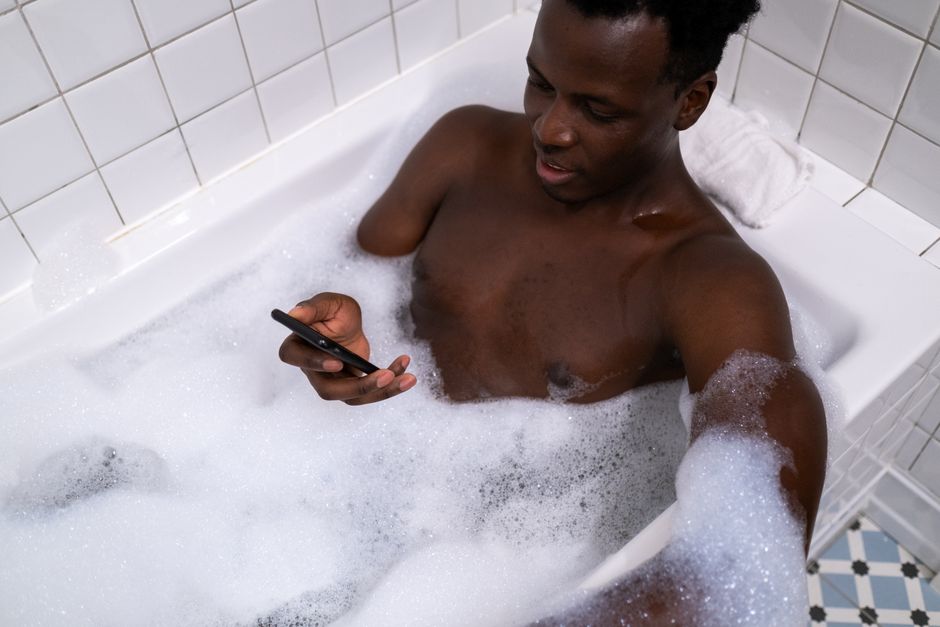Homem relaxando no banho de banheira enquanto usa o celular, criando uma atmosfera de lazer e bem-estar.