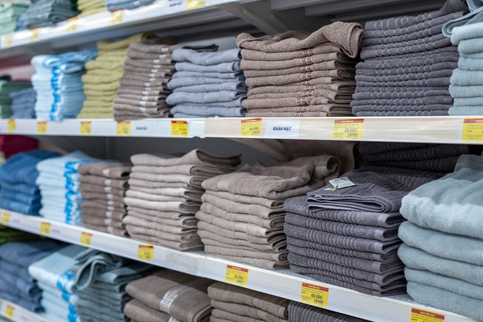 Imagem de prateleiras de toalhas ou roupas de tecido organizadas por cores em uma loja de varejo.
