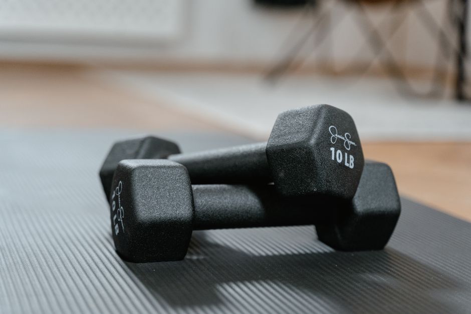 Imagem de um par de halteres de 10 libras em um ambiente de treino, representando exercícios físicos e hipertrofia muscular.