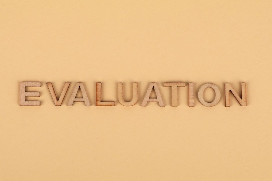 Imagem de letras de madeira formando a palavra 'EVALUATION' em um tom neutro, simbolizando análise ou avaliação de processos ou desempenho.