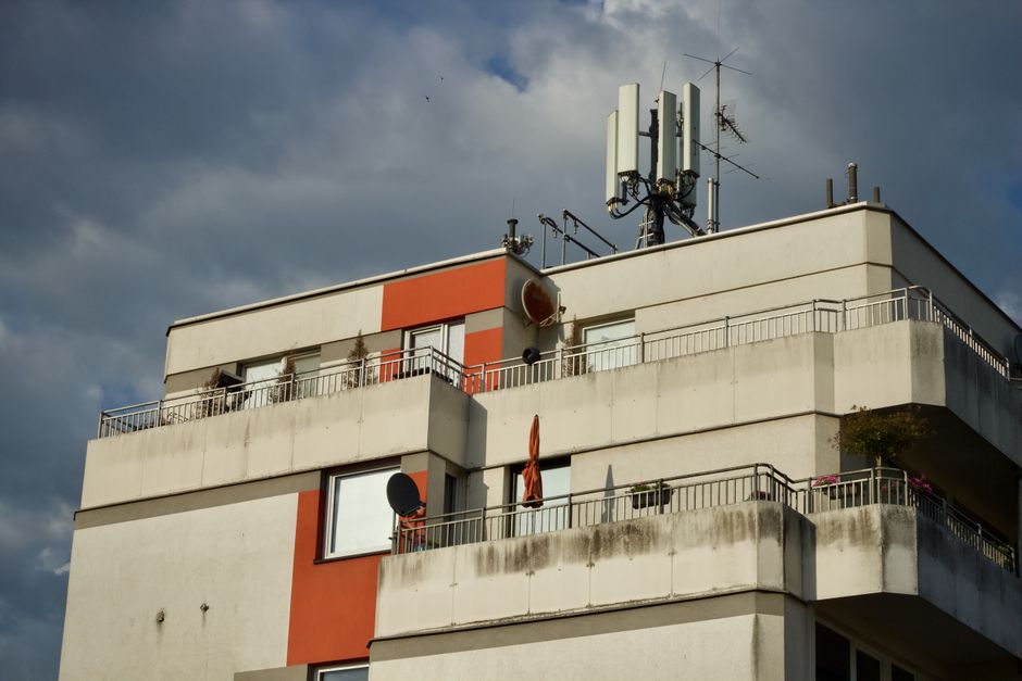 Imagem de um edifício residencial com antenas e satélites no topo, sob céu nublado, representando tecnologia e comunicação urbana.