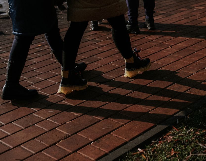 Foto de pessoas caminhando sobre calçada de tijolos, sugerindo movimento e vida urbana em ambiente noturno.