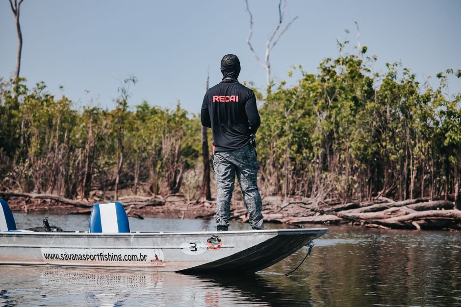 Pessoa em um barco de pesca explorando um ambiente natural com vegetação ao redor.