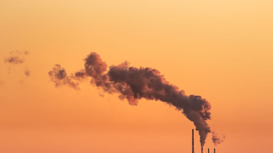 Imagem de uma fumaça escura saindo de fábricas ao entardecer, simbolizando questões ambientais e sustentabilidade industrial.