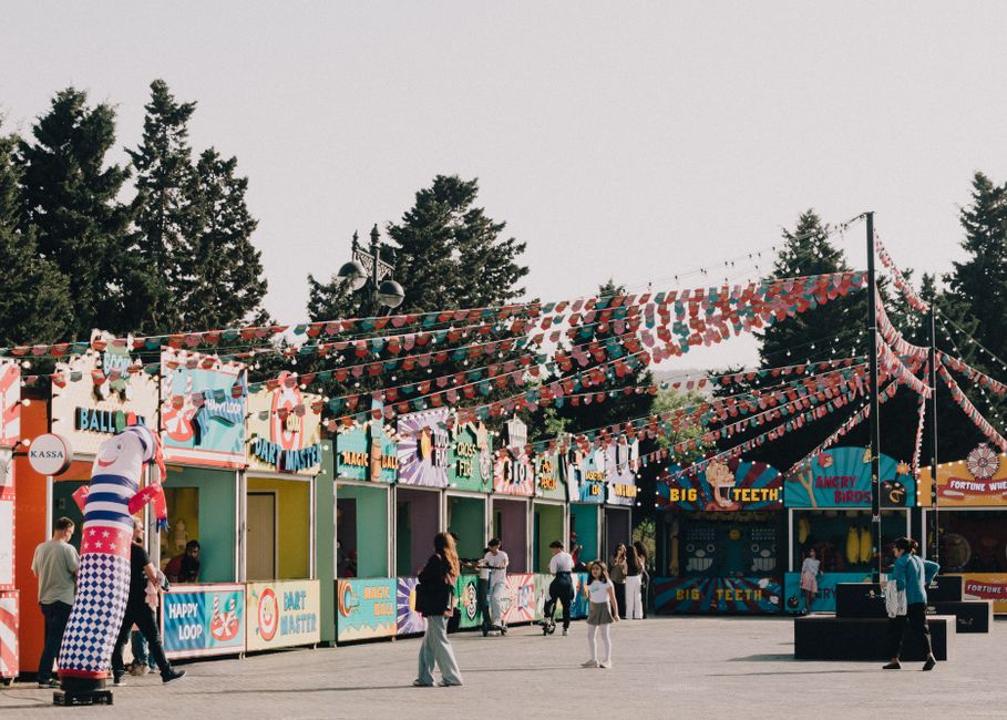 Imagem de parque de diversões ao ar livre, com barracas decoradas e pessoas aproveitando o espaço, ideal para artigos sobre lazer, eventos ou entretenimento ao ar livre.