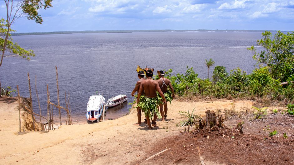 Homens indígenas caminhando em direção ao rio, evidenciando cultura e conexão com a natureza.
