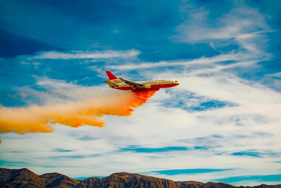 Avião deixando uma trilha de fumaça colorida sobre as montanhas, simbolizando inovação e impacto nos setores de transporte e logística.