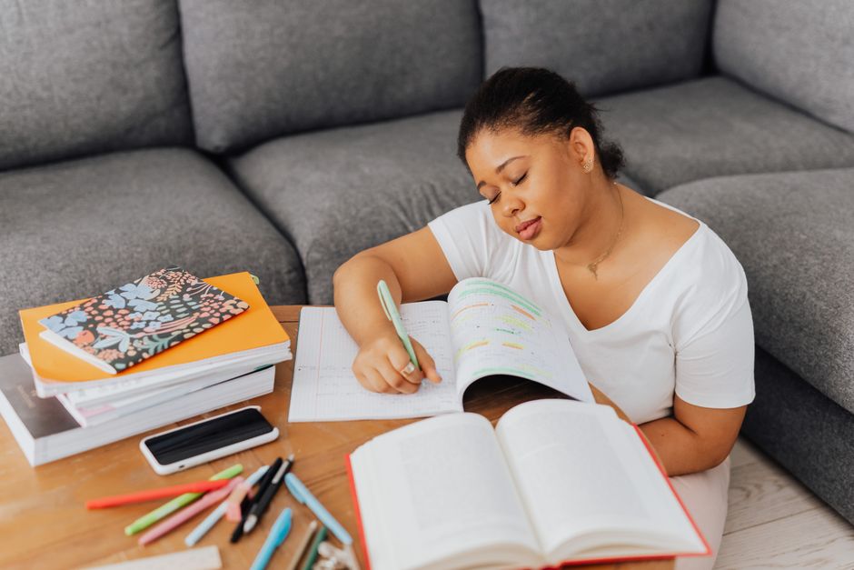 Mulher estudando e fazendo anotações de forma concentrada em um ambiente doméstico.