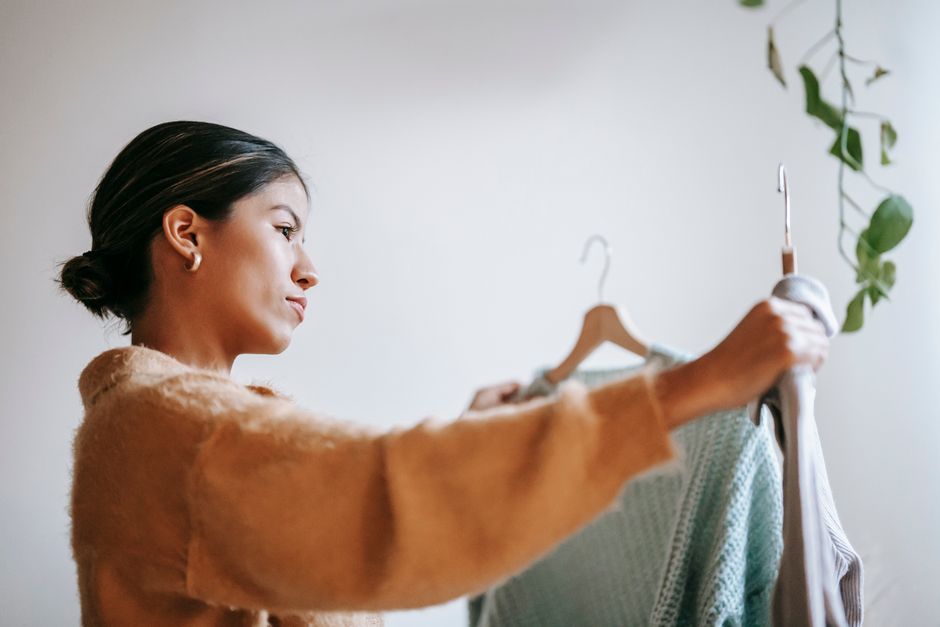 Mulher avaliando roupas em cabide, simbolizando sustentabilidade e consumo consciente.