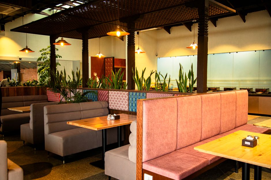 Ambiente de restaurante ou café com decoração acolhedora, iluminação suave e áreas de descanso com assentos confortáveis.