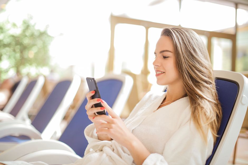 Mulher relaxada usando smartphone em ambiente de lazer, transmitindo bem-estar e conexão digital.