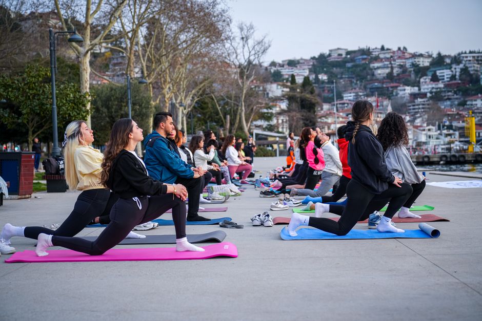Grupo de pessoas participando de aula de yoga ao ar livre em um cenário urbano com moradias ao fundo.