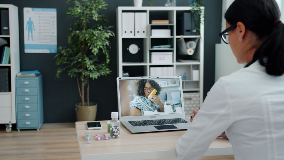 Profissional de saúde realizando consulta médica virtual com paciente em ambiente de escritório bem organizado.