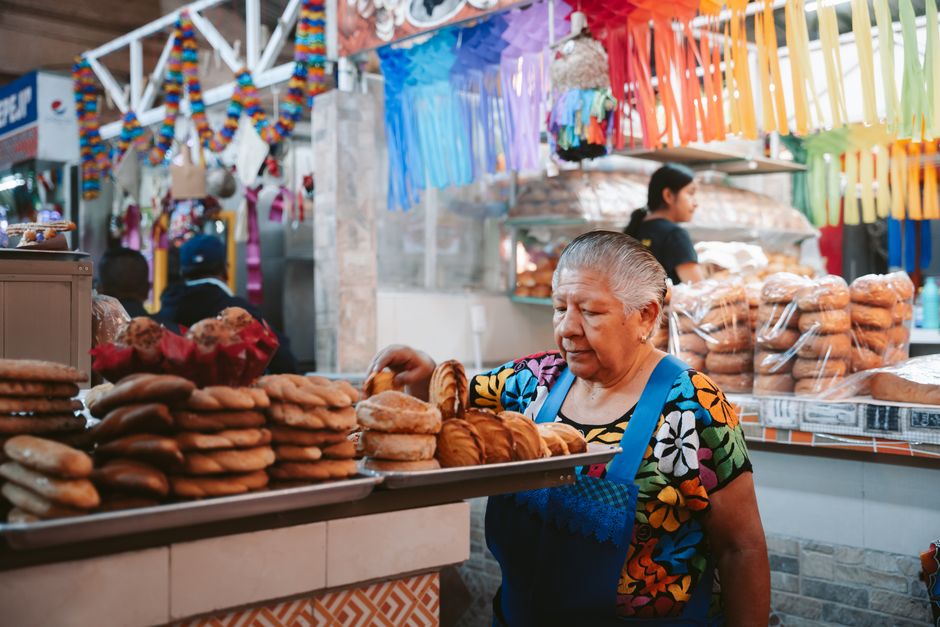 Mulher idosa vendendo pães em feira popular, destacando tradição e comércio local.