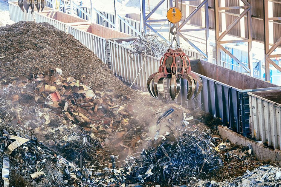 Imagem de uma operação de reciclagem de lixo metálico, com uma máquina de braço robótico manipulando sucata em um ambiente industrial.