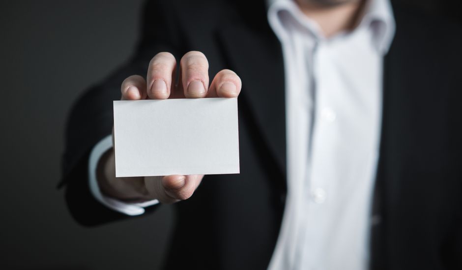 Homem de terno sostendo um cartão em um fundo escuro, simbolizando negócios e comunicação empresarial.