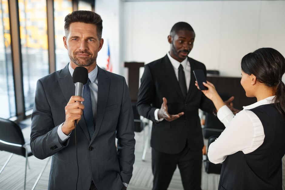 Homem apresentando discurso ou anúncio em evento corporativo ou de negócios.