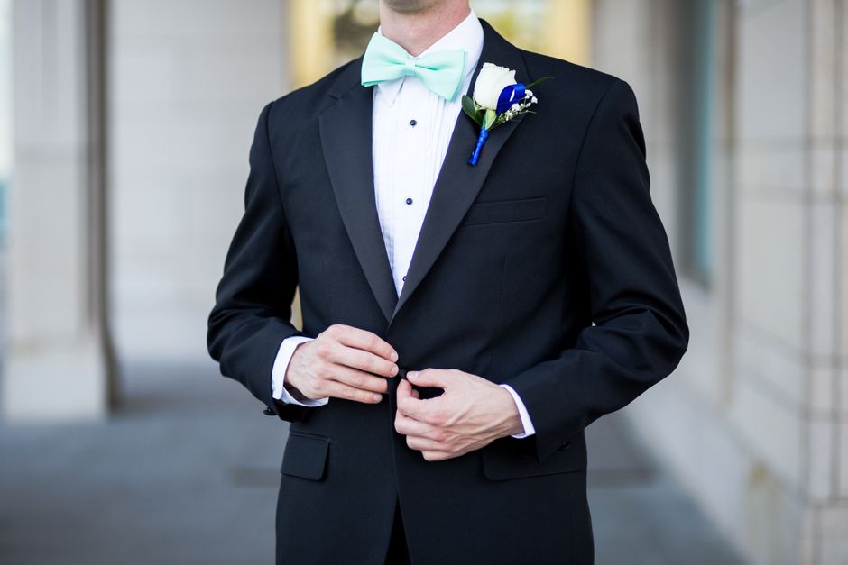 Homem vestindo terno de casamento com boutonnière e gravata borboleta, pronto para um evento formal ao ar livre.