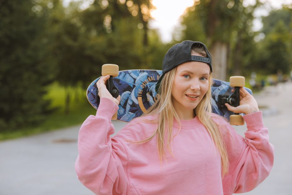 Jovem andando de skate ao ar livre durante o pôr do sol, em um ambiente natural com árvores ao fundo.