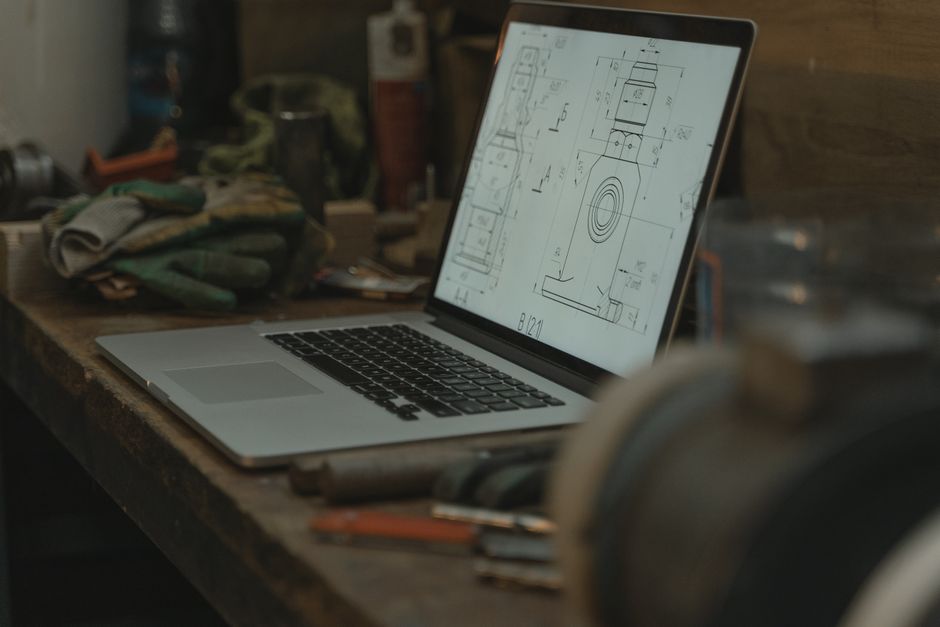 Imagem de uma bancada de trabalho com um laptop exibindo desenhos técnicos, refletindo um ambiente de desenho ou projeto de engenharia ou arquitetura.