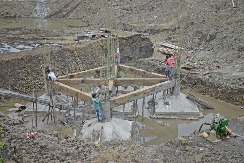 Obras de fundação de uma ponte em andamento, com trabalhadores construindo a estrutura de suporte no local da construção.